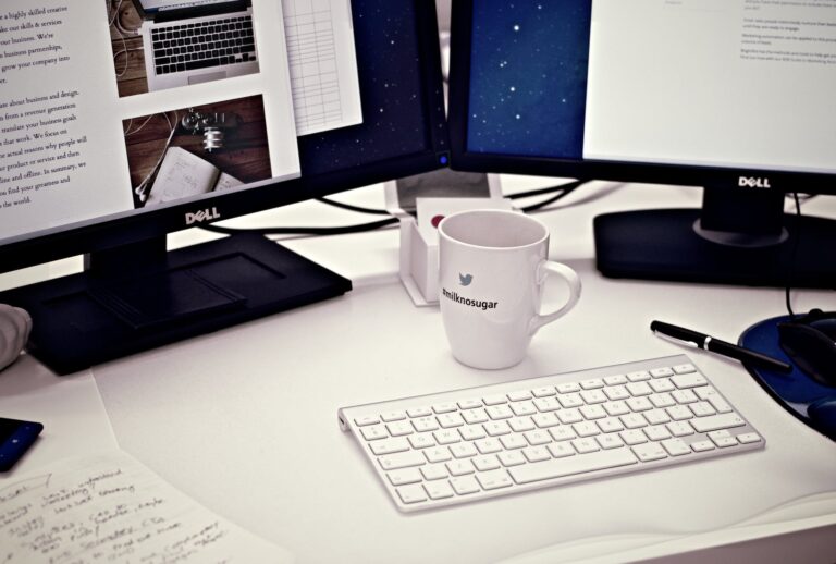 white ceramic mug between apple magic keyboard and two flat screen computer monitors